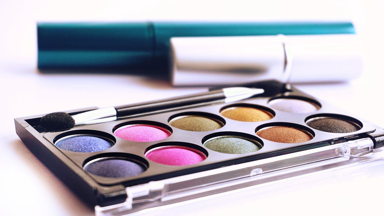 about-us-02 Close-up of colorful eyeshadow palette with brush, ideal for fashion and beauty themes.