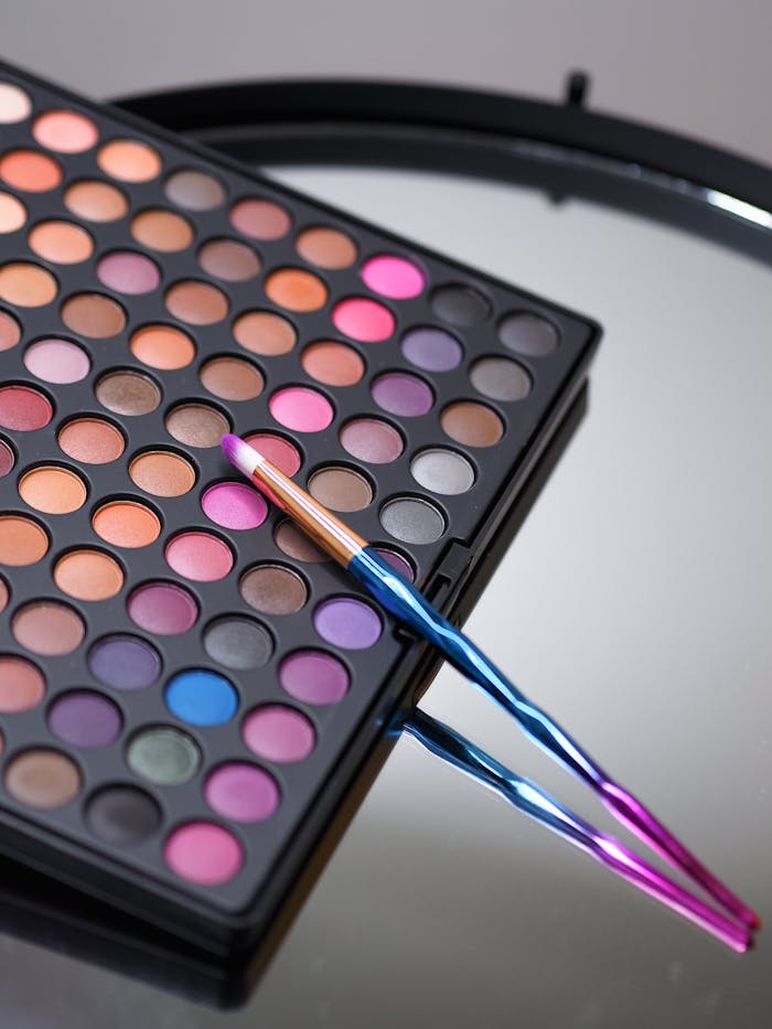 our-story-02 A vibrant makeup palette and brush displayed on a reflective surface.