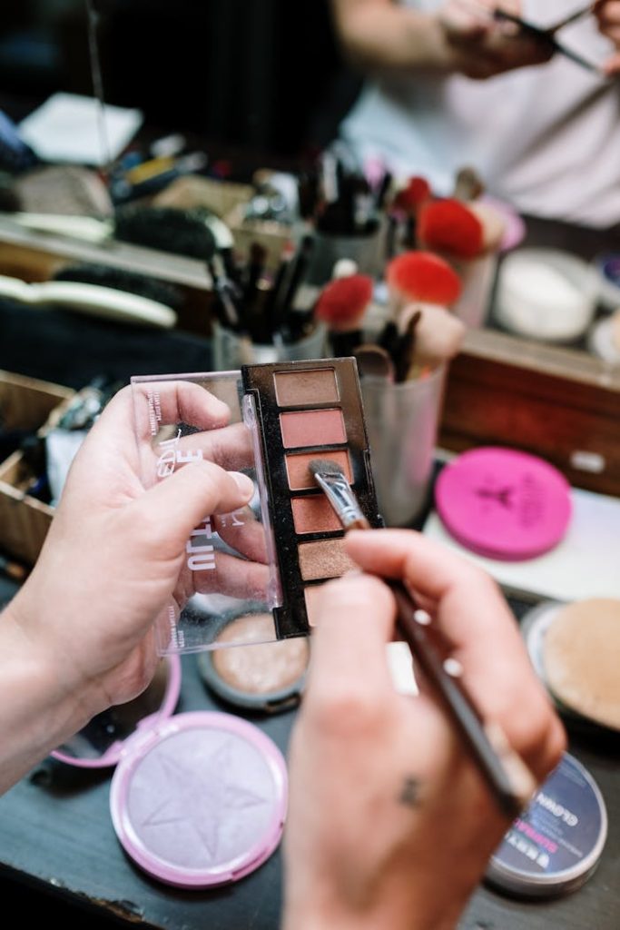 Close-up of a makeup artist working with an eyeshadow palette and brush, highlighting beauty and cosmetics.