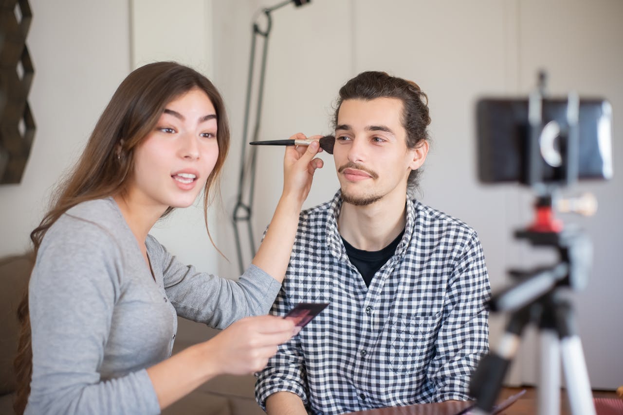 gallery-04 Woman applying makeup to a man during a tutorial session indoors.